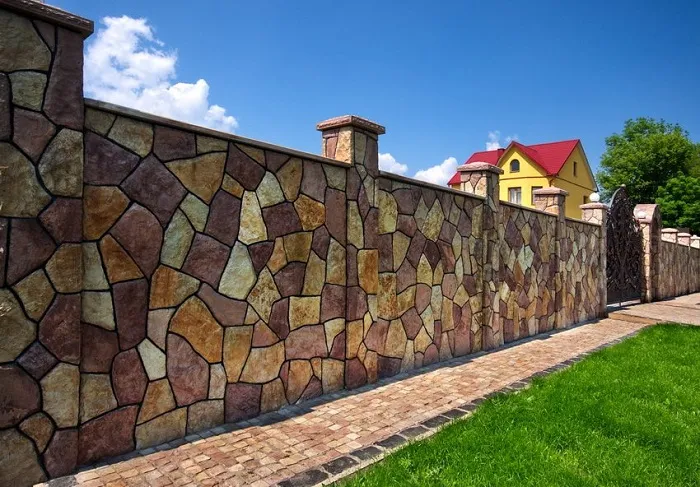С виду забор из разных цветных камней, но нет. Это просто на бетоне сделали дизайн дикого разноцветного камня различных размеров.