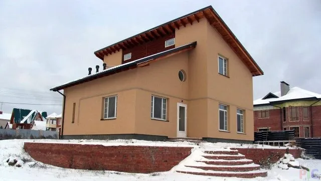 Двухэтажный дом с комбинированной крышей на заснеженном участке